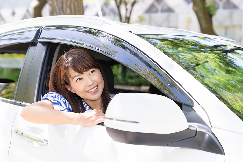 白い車に乗り窓から顔を出す若い女性